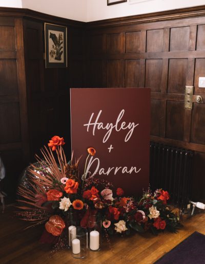 rich toned welcome sign stand sat inside the entrance of Acnagairn Castle with rich toned florals at the base