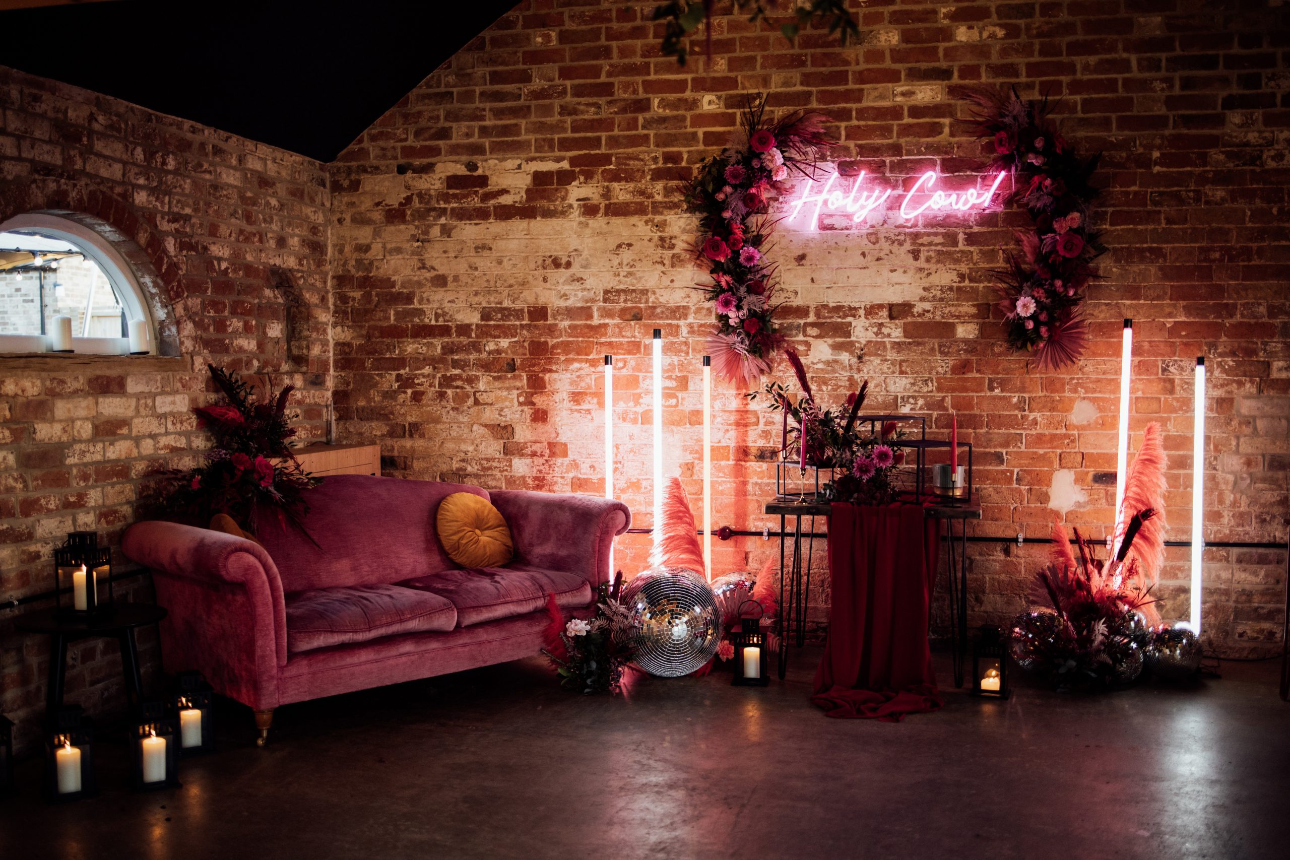 the old cow shed barn filled with pink sofa, floral backdrop and holy cow pink neon. With disco balls and flowers on the floor