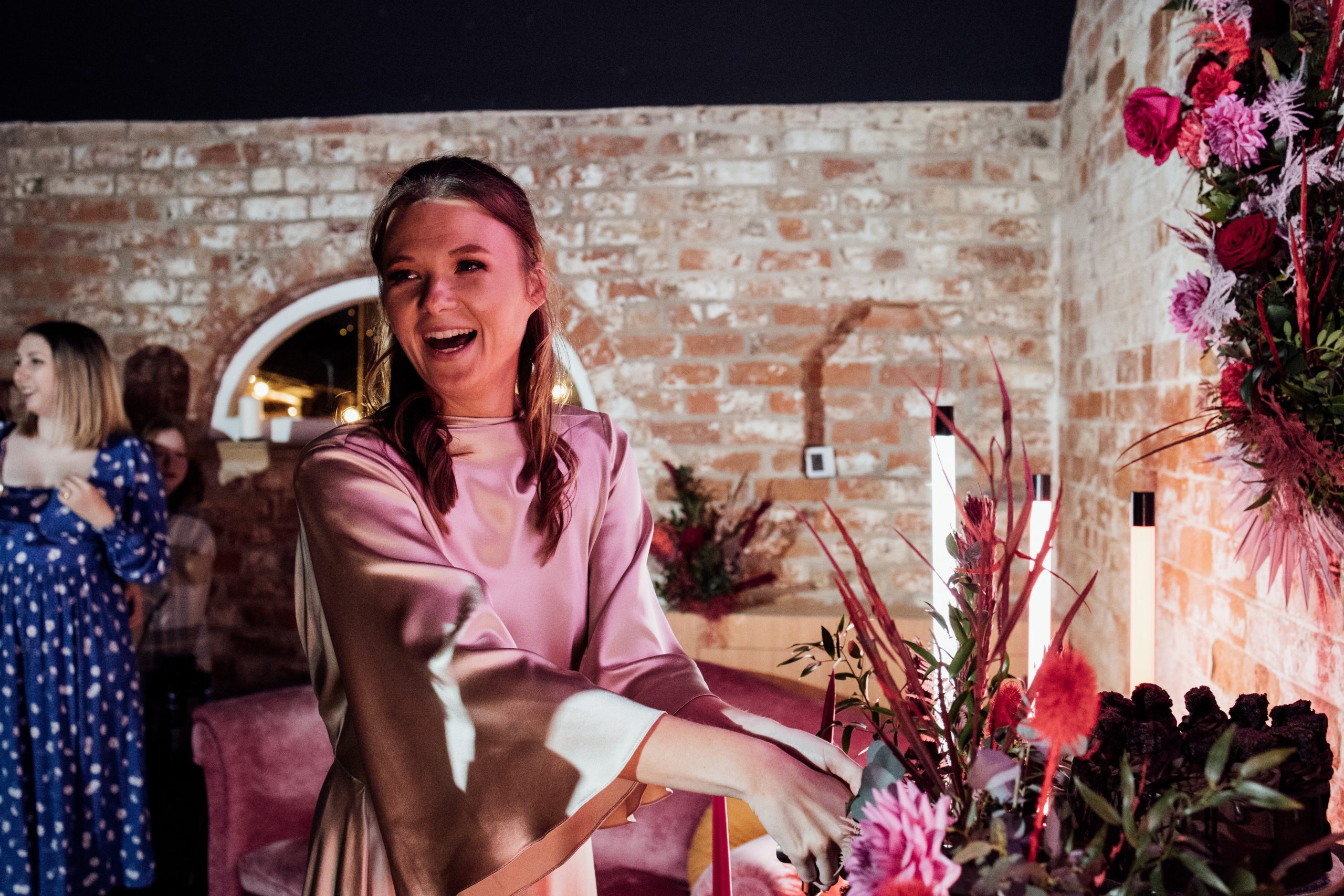 A happy bride with pink florals and neon stands in a barn venue