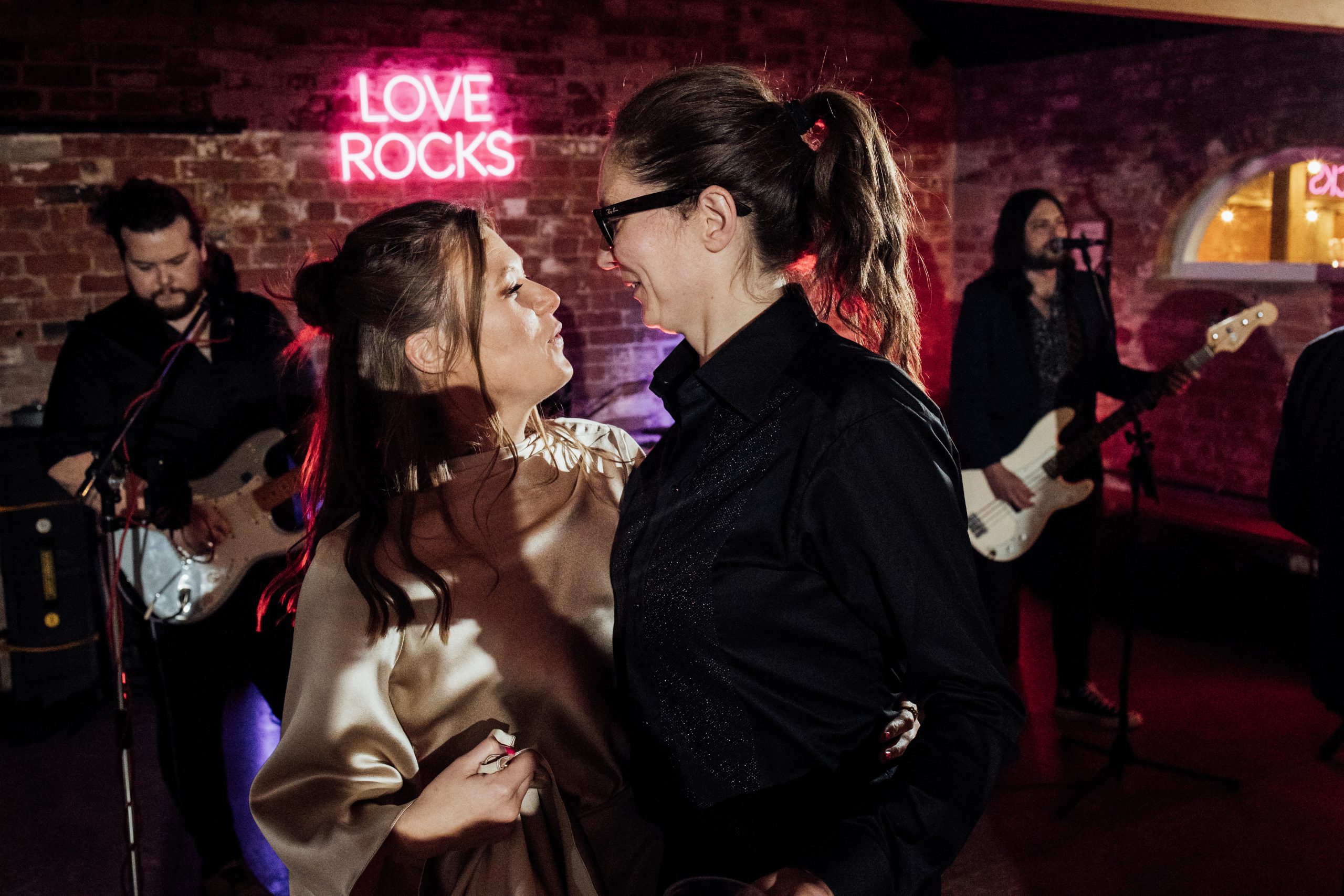 Two brides dancing infront of a love rocks neon at the old cow shed