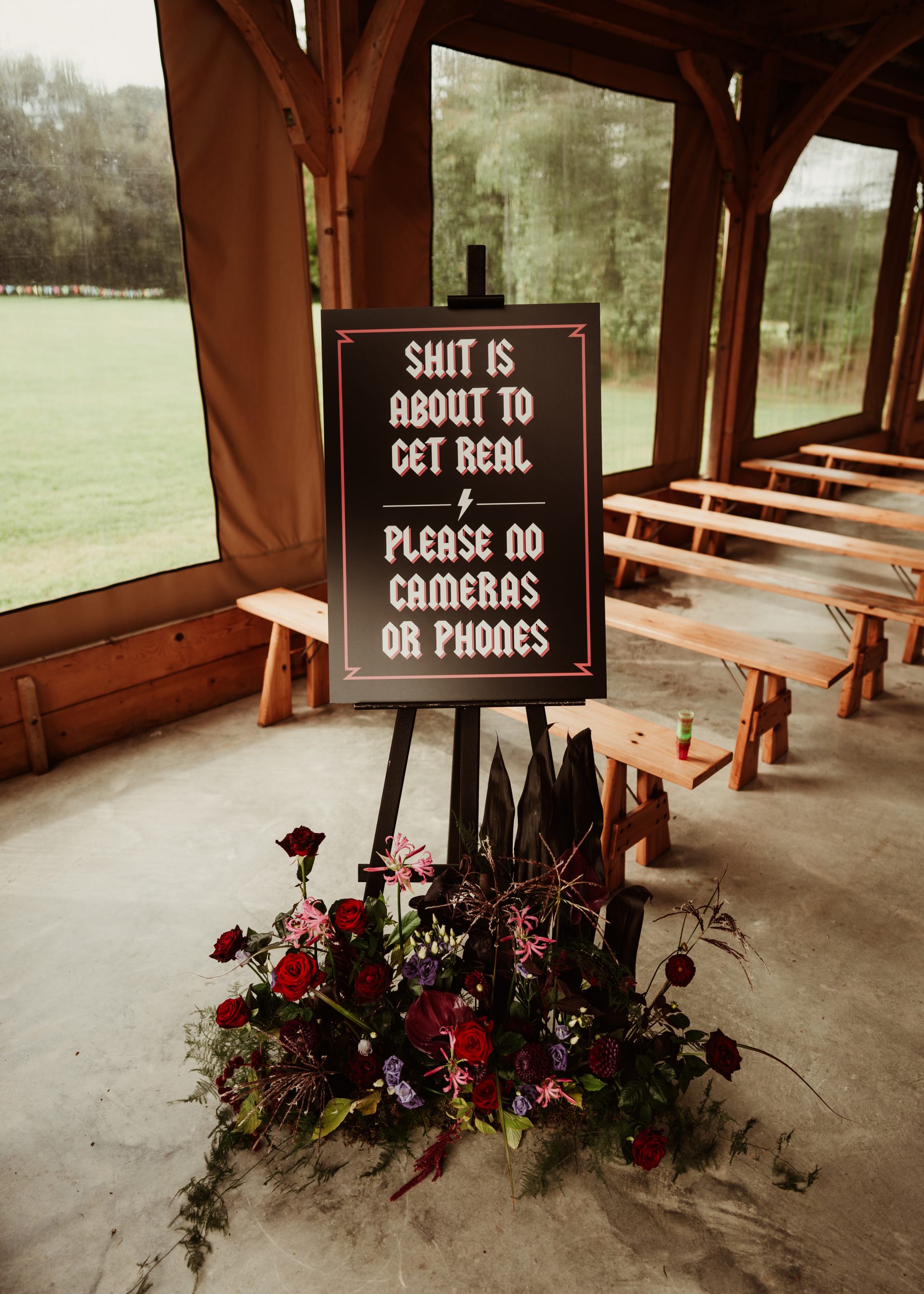 a alternative welcome sign asking couples to not use their phones styled on a black easel with a floral meadow along the floor