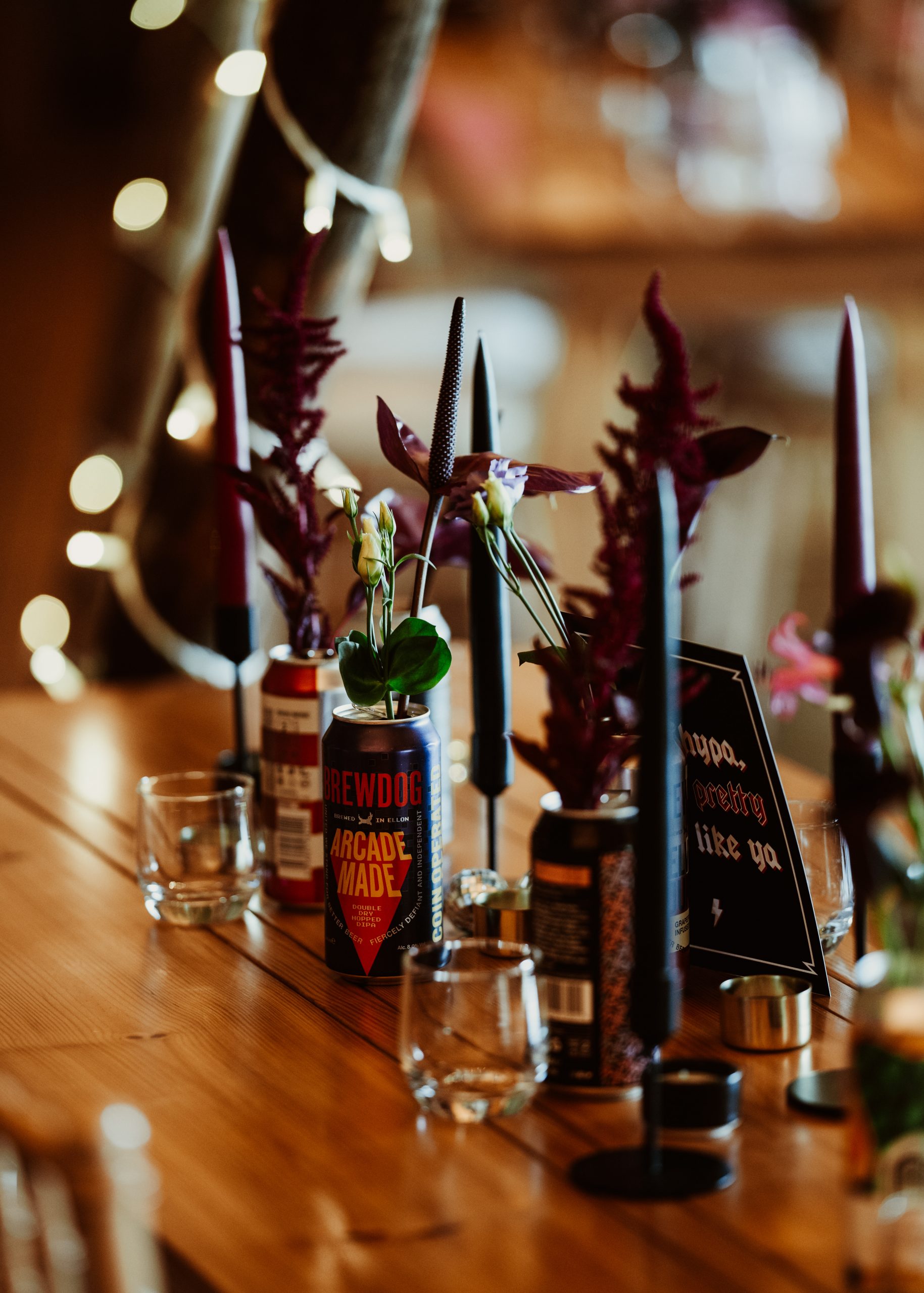 a wedding table filled with beer cans filled with flowers and a display of clack and red candles