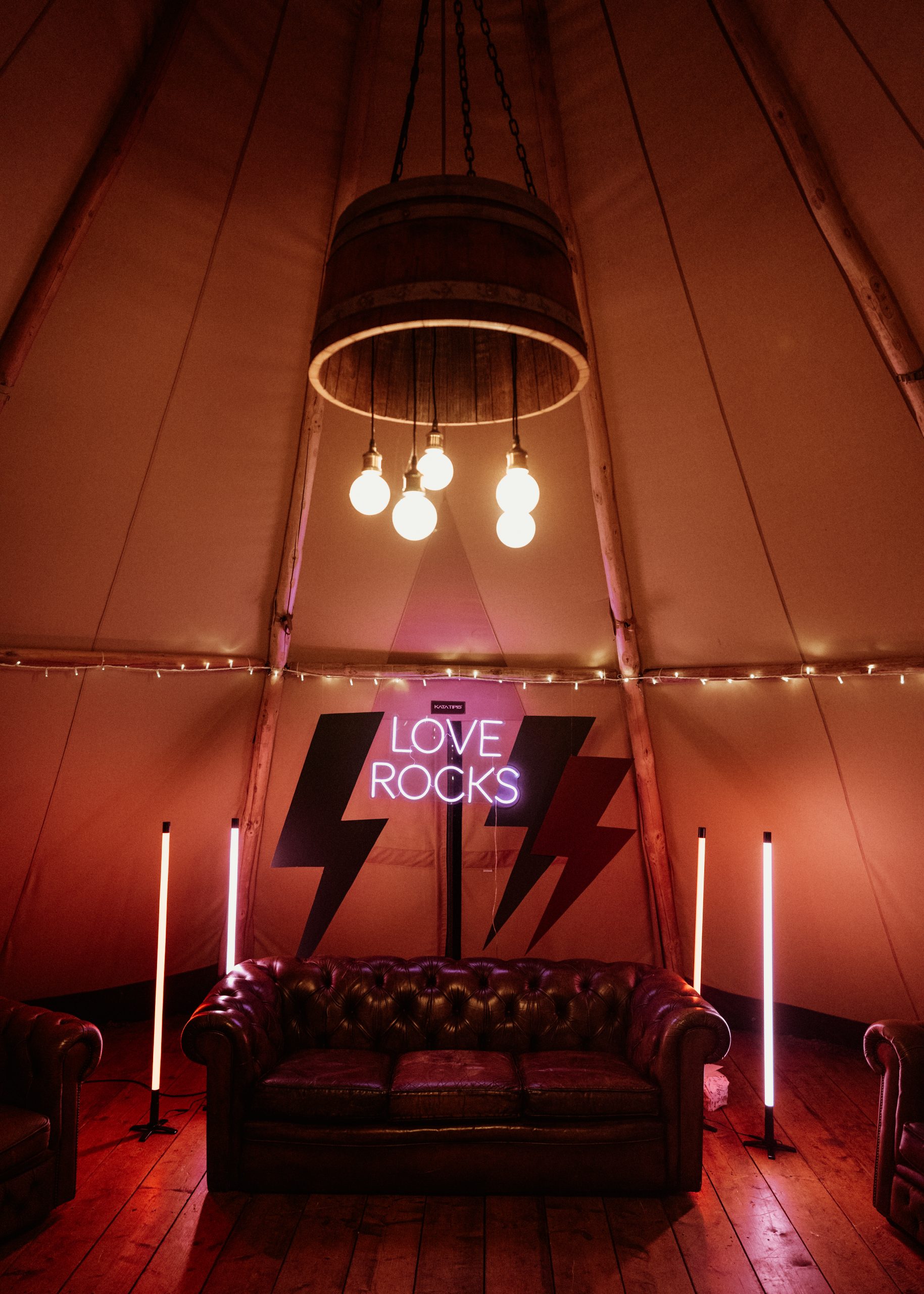a tipi cosy section with vintage sofa, love rock pink neon, neon strips and hanging lightening bolts