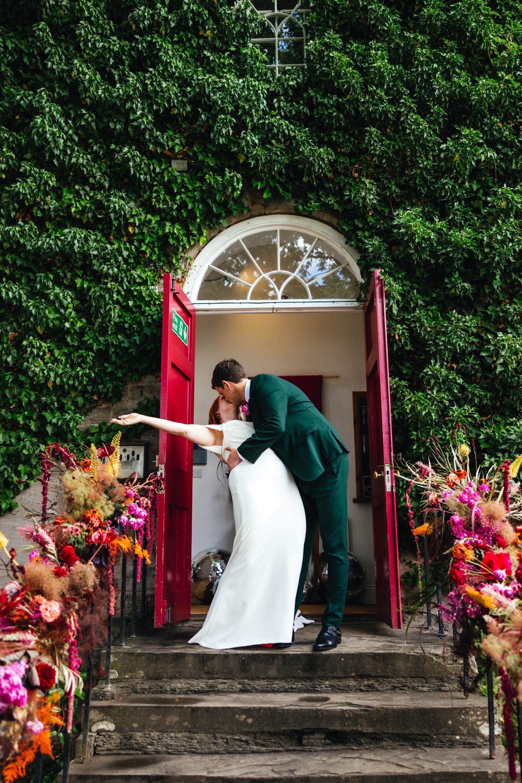 Bride and Groom kissing at the front doors of The Globe in Hay. Surrounded by colourful flowers